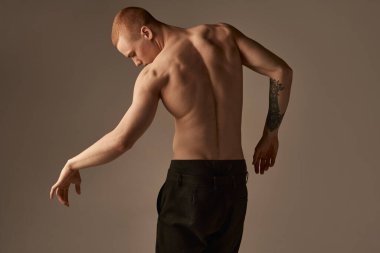 Gri stüdyo arka planında pantolonsuz poz veren yakışıklı kızıl saçlı genç adam portresi. Kaslı vücut şekli. Rahatlayın. Erkeklerin sağlık ve güzellik anlayışı, vücut ve cilt bakımı, fitness. Vücut sanatı