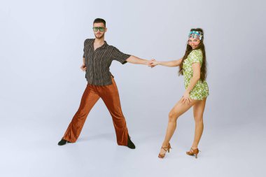 Gri arka planda izole bir şekilde dans eden eski sahne kostümlü aktif erkek ve kadının dinamik stüdyo görüntüleri. 70 'ler moda, hobi, yaratıcılık, hippi yaşam tarzı, Amerikan kültürü