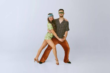 İyi titreşimler. Tarz sahibi genç bir adam ve modaya uygun retro kıyafetler içindeki güzel bir kadın. Disko dansçıları gri stüdyo arka planında izole edilmiş. 70 'ler moda, hobi, yaratıcılık, hippi yaşam tarzı, Amerikan kültürü