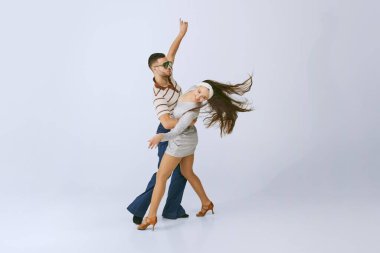 Hareket halinde. Gümüş elbiseli güzel bir kız ve gri stüdyo arka planında izole bir şekilde dans eden şık bir adam. 70 'ler moda, hobi, yaratıcılık, hippi yaşam tarzı, Amerikan kültürü