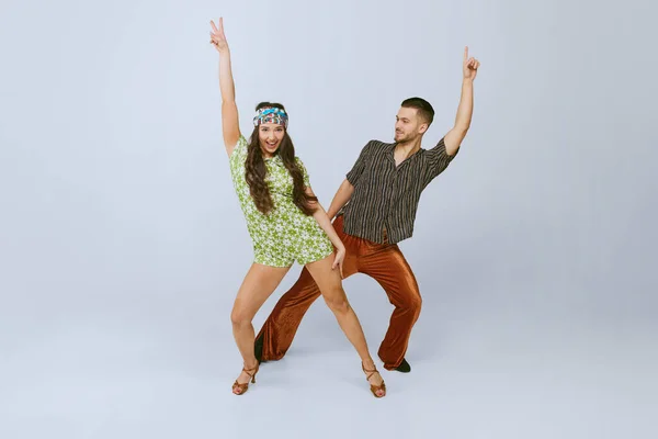 Stylish emotional young man and woman in fashionable retro outfits dancing disco dance isolated over grey studio background. 70s fashion, hobby, creativity, hippie lifestyle, American culture