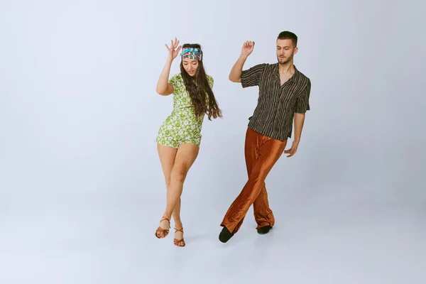 Expression. Stylish young man and woman in fashionable retro outfits dancing disco dance isolated over grey studio background. 70s fashion, hobby, creativity, hippie lifestyle, American culture