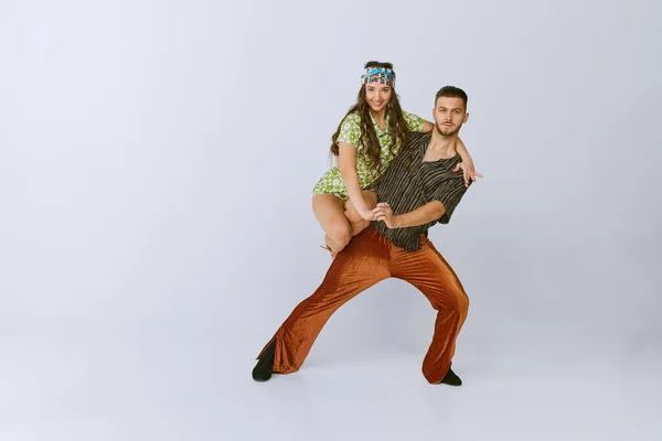Impressive position. Beautiful. talented young man and woman, disco dancers dancing isolated over grey studio background. 70s fashion, hobby, creativity, hippie lifestyle, American culture