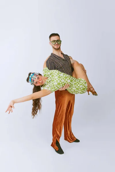 Attractive dance. Stylish young man and woman in bright retro outfits dancing disco dance isolated over grey studio background. 70s fashion, hobby, creativity, hippie lifestyle, American culture