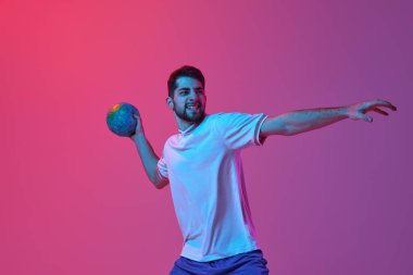 Hırslar. Genç bir adam, profesyonel hentbol antrenmanı, neon ışıklarıyla izole edilmiş pembe arka planda oynuyor. Spor, eylem, hareket, şampiyonluk, spor yaşam tarzı kavramı