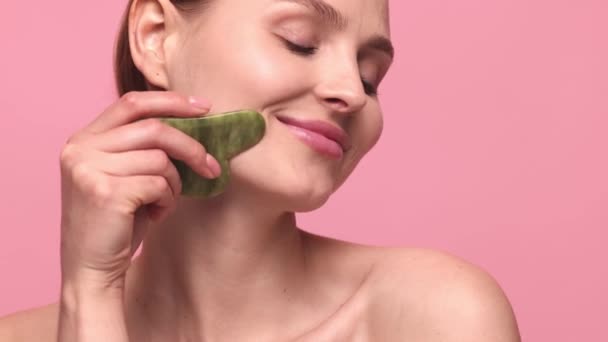 顔を上げろリフティング ピンクのスタジオの背景に隔離されたガッシュで顔のマッサージを行う明確な肌を持つ美しい若い女の子 スキンケア 自然美 化粧品の概念 — ストック動画