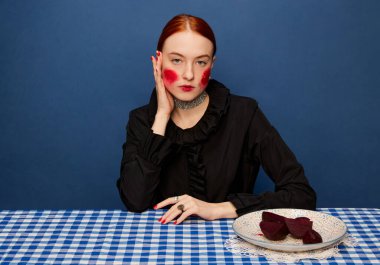 Natural vitamins. Young beautiful girl with beets on retro tablecloth over blue studio background. Food pop art photography. Complementary colors. Concept of art, beauty, food. Copy space for ad, text