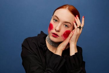Beetroot cheeks. Young beautiful girl eating beet over blue studio background. Food pop art photography. Complementary colors. Concept of art, beauty, food. Copy space for ad, text.