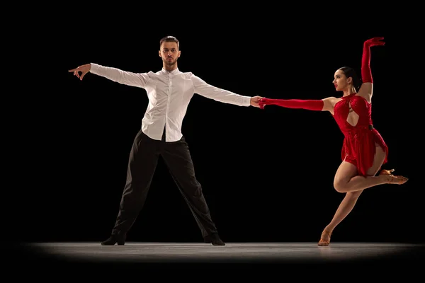 Professional dancers. Art. Young man and woman in stylish stage costumes dancing tango, ballroom over black background. Concept of hobby, lifestyle, action, beauty of movements, emotions