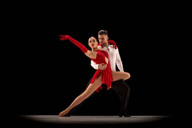 Passionate attractive young man and woman, professional ballroom dancers dancing tango over black background. Concept of hobby, lifestyle, action, beauty of movements, emotions, fashion, art