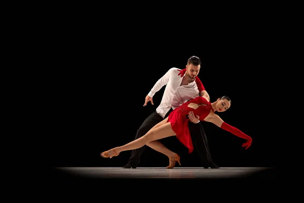 Beautiful, talented, attractive young man and woman, professional dancers performing, dancing tango over black background. Concept of lifestyle, action, beauty of movements, emotions, fashion, art