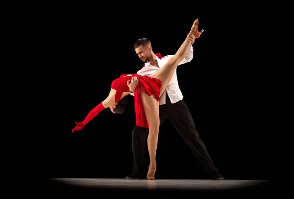 Talented performers. Beautiful young people, man and woman dancing tango over black studio background. Concept of hobby, lifestyle, action, beauty of movements, emotions, fashion, art
