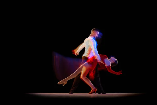 Man and woman, professional dancers performing ballroom, tango over black background with mixed neon lights. Concept of hobby, lifestyle, action, beauty of movements, emotions, fashion, art