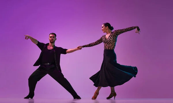 Talented young man and woman, professional dancers performing tango over purple background on neon lights. Concept of hobby, lifestyle, action, beauty of movements, emotions, fashion, art