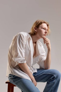 Looking thoughtful. Portrait of young redhead man posing in white shirt and jeans over grey studio background. Concept of mens health, body and skin care, hygiene and male cosmetology