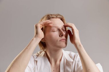 Pale skin color. Portrait of young redhead man posing in white shirt over grey studio background. Casual mans fashion. Concept of mens health, body and skin care, hygiene and male cosmetology