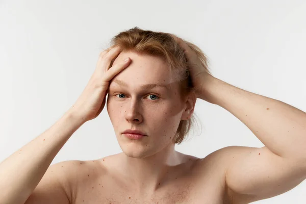 Self-care. Portrait of young redhead man posing shirtless, doing hairstyle after shower over grey studio background. Concept of mens health, body and skin care, hygiene and male cosmetology