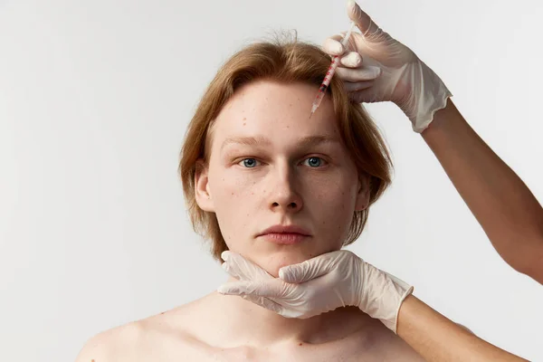 Reducing forehead wrinkles with botox. Young redhead man having cosmetological injections. Male model posing against grey background. Mens health, cosmetology, plastic surgery, kin care, medicine