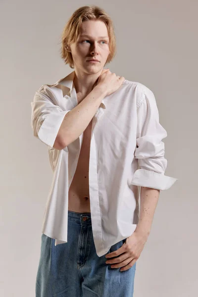 Portrait of young redhead man posing in white shirt and jeans over grey studio background. Casual male outfit. Concept of mens health, body and skin care, hygiene and male cosmetology