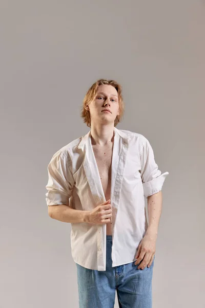 Wellbeing, self-acceptance. Portrait of young redhead woman posing in white shirt and jeans over grey studio background. Concept of mens health, body and skin care, hygiene and male cosmetology