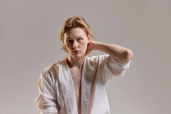 Portrait of young redhead man posing in white shirt over grey studio background. Casual mans fashion, comfort and wellness. Concept of mens health, body and skin care, hygiene and male cosmetology