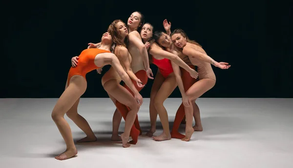 Flexible aesthetic movements, experimental dance. Group of young beautiful girls performing over black studio background. Concept of art, movement, youth, fashion, artistic lifestyle