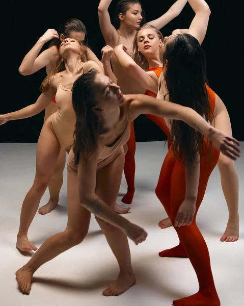 Chaotic movements. Group of artistic talented young girls performing experimental dance style on stage over black background. Concept of art, movement, youth, fashion, flexibility, inspiration