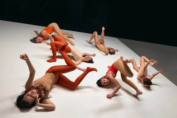 Experimental, contemporary dance style aesthetics. Young girls in bodysuits performing on stage on black background. On own position. Concept of art, movement, youth, fashion, flexibility, inspiration