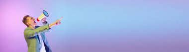 News. Sales. Young handsome man in stylish jacket emotionally shouting in megaphone on purple background in neon light. Concept of emotions, lifestyle, youth, modern fashion. Banner. Copy space for ad