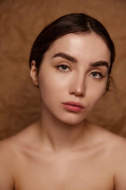 No makeup look. Beautiful young brunette girl with healthy smooth well-kept skin over brown studio background. Concept of natural beauty, skincare, cosmetology, plastic surgery, health