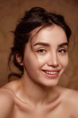 Tenderness and purity. Beautiful smiling young brunette girl with clear healthy skin posing over brown studio background. Concept of natural beauty, skincare, cosmetology, plastic surgery, health, spa
