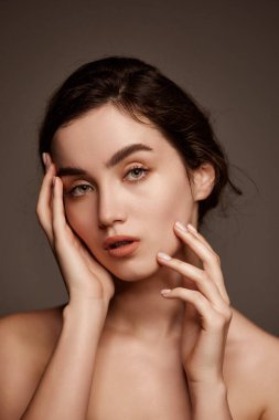 Tenderness. Portrait of young beautiful girl with brown hair and nude makeup style posing over dark grey studio background. Concept of natural beauty, skincare, cosmetology, plastic surgery, health