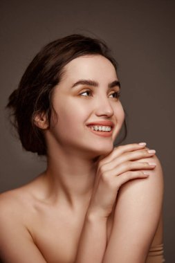 Attractive smile, tenderness. Portrait of young beautiful girl with brown hair posing over dark grey studio background. Concept of natural beauty, skincare, cosmetology, plastic surgery, health