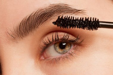 Close-up image of female face, eye and eyebrow. Applying mascara on eyelashes to make them look longer. Concept of natural beauty, skincare, cosmetology, plastic surgery, health