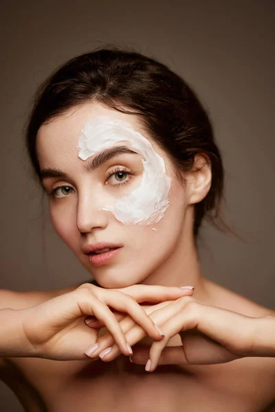 Cosmetics face care. Portrait of young brunette beautiful girl with face mask on well--kept skin posing over dark grey studio background. Concept of natural beauty, skincare, cosmetology, health