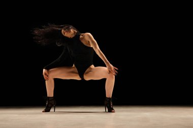 Sensuality. Passionate young woman dancing stiletto dance in bodysuit and heels over black background. Concept of contemporary dance style, art, aesthetics, hobby, creative lifestyle