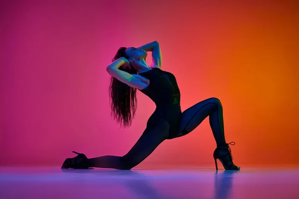Flexibility and passion. Young woman dancing high heel, contemp dance over gradient pink red studio background in neon light. Contemporary dance style, art, aesthetics, hobby, creative lifestyle