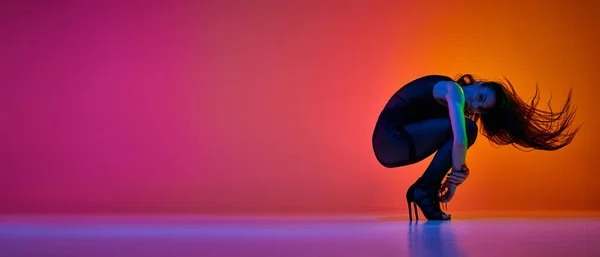 若い女性は ネオンの光の中でグラデーションピンクオレンジ色のスタジオの背景の上に踊るために ハイヒールを踊ります コンテンポラリーダンスのスタイル アート 創造的なライフスタイル バナーだ 広告のコピースペース — ストック写真