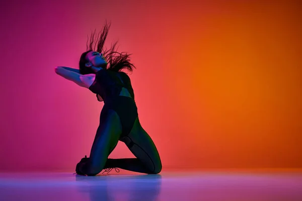 動きによる自己表現 ネオンライトでグラデーションピンクオレンジ色のスタジオの背景に高いヒールダンススタイルを踊る若い女性 コンテンポラリーダンススタイル アート 創造性 — ストック写真