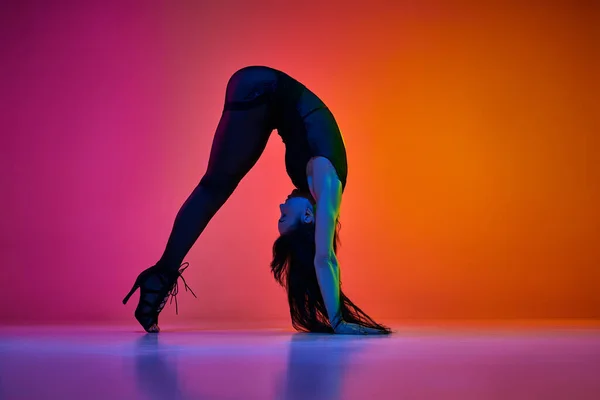 Flexibility. Young woman dancing modern dance style over gradient pink orange studio background in neon light. Concept of contemporary dance style, art, aesthetics, hobby, creative lifestyle
