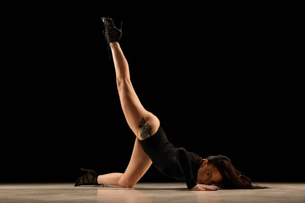 Passionate movements. Young flexible woman in bodysuit and heels dancing, performing over black background. Concept of contemporary dance style, art, aesthetics, hobby, creative lifestyle