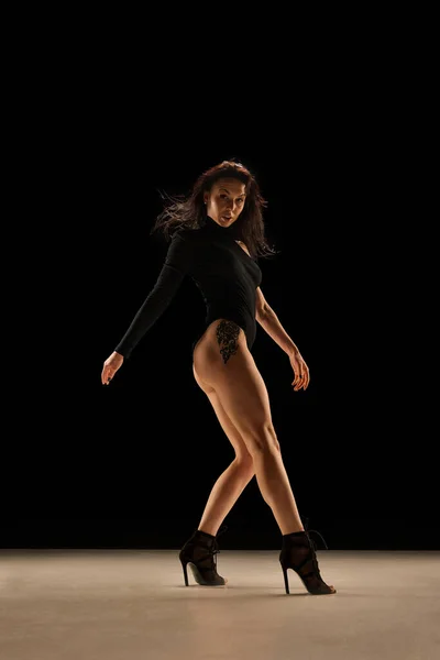 Step by step. Young woman in bodysuit and heels dancing, performing over black background. Concept of contemporary dance style, art, aesthetics, hobby, creative lifestyle, emotions