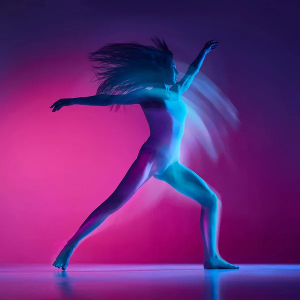 Young artistic woman in bodysuit dancing over gradient pink studio background in neon with mixed lights. Concept of contemporary dance style, art, aesthetics, hobby, creative lifestyle