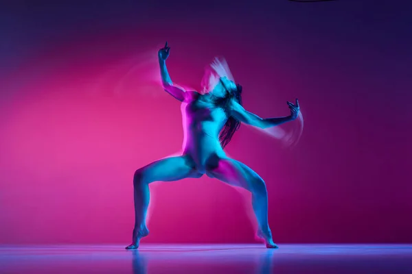 Muscular flexible young woman dancing contemp over gradient pink studio background in neon with mixed lights. Concept of contemporary dance style, art, aesthetics, hobby, creative lifestyle