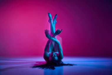 Hidden feelings. Young talented woman dancing, performing on gradient pink studio background in neon with mixed lights. Concept of contemporary dance style, art, aesthetics, hobby, creative lifestyle