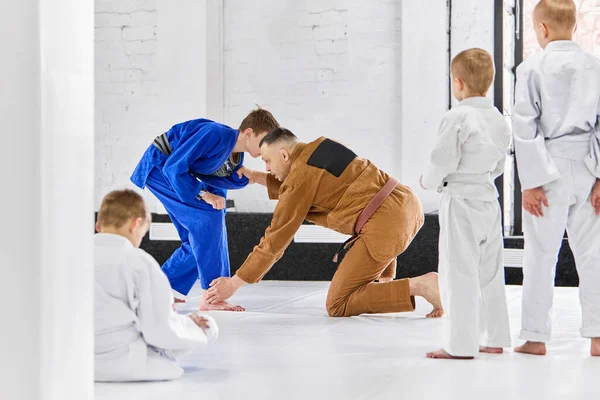 Teacher showing mix fight tricks to children, learning judo, jiu-jitsu fight activity. Sportive active lifestyle. Concept of martial arts, combat sport, sport education, childhood