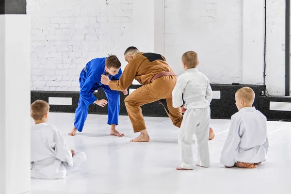 Man, professional sport coach teaching boys, children judo, jiu-jitsu fight activity. Professional athletes and kids. Concept of martial arts, combat sport, sport education, childhood