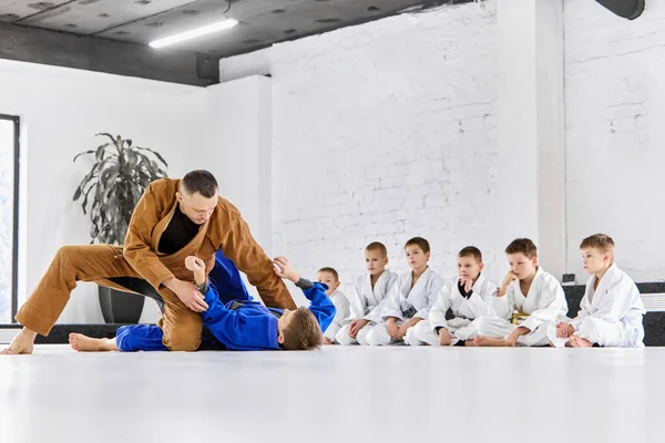 Teacher, professional judo, jiu jitsu coach training, teaching kinds, boys to fight. Children learning indoors. Concept of martial arts, combat sport, sport education, childhood