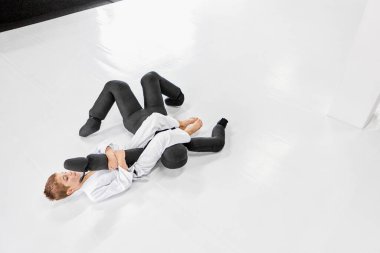 Little boy, child in white kimono practising, training judo, jiu-jitsu exercises with sport mannequin. Concept of martial arts, combat sport, sport education, childhood, hobby