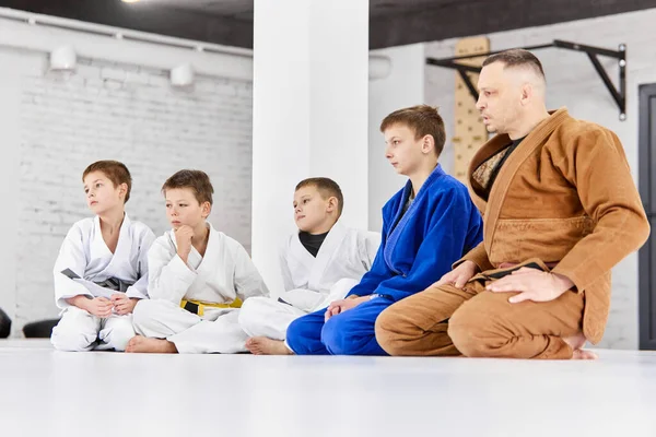 気をつけて 柔道のコーチ 少年と座って柔術 白い着物の子供たち 運動技術を見て 武道の概念 戦闘スポーツ スポーツ教育 子供時代 — ストック写真